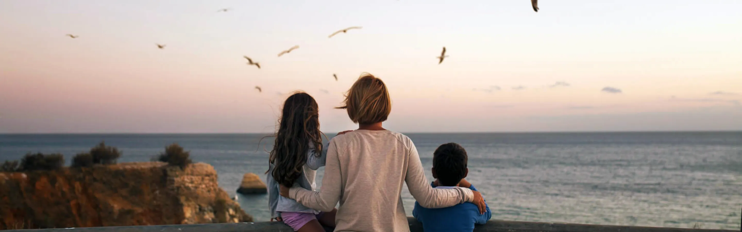 Woman and two children watching the sunset and a group of flying seagulls over the sea