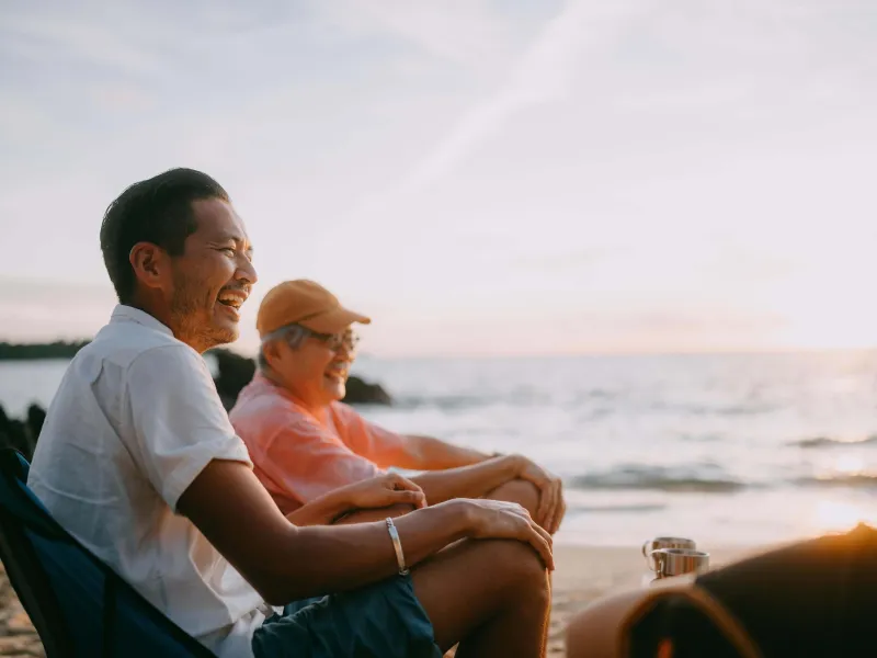 Father and son sitting on chairs and smiling at the beach in the afternoon sun