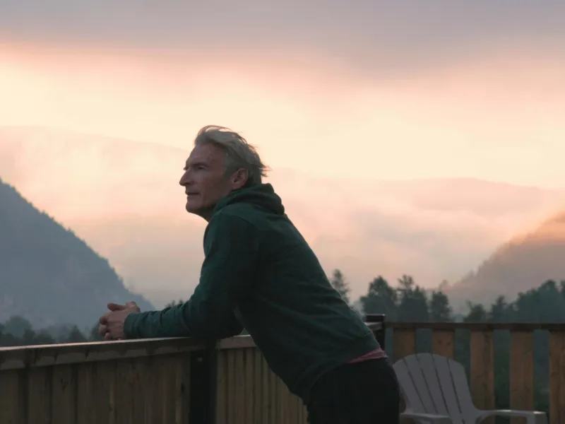 Older man on balcony watching sunset over mountains