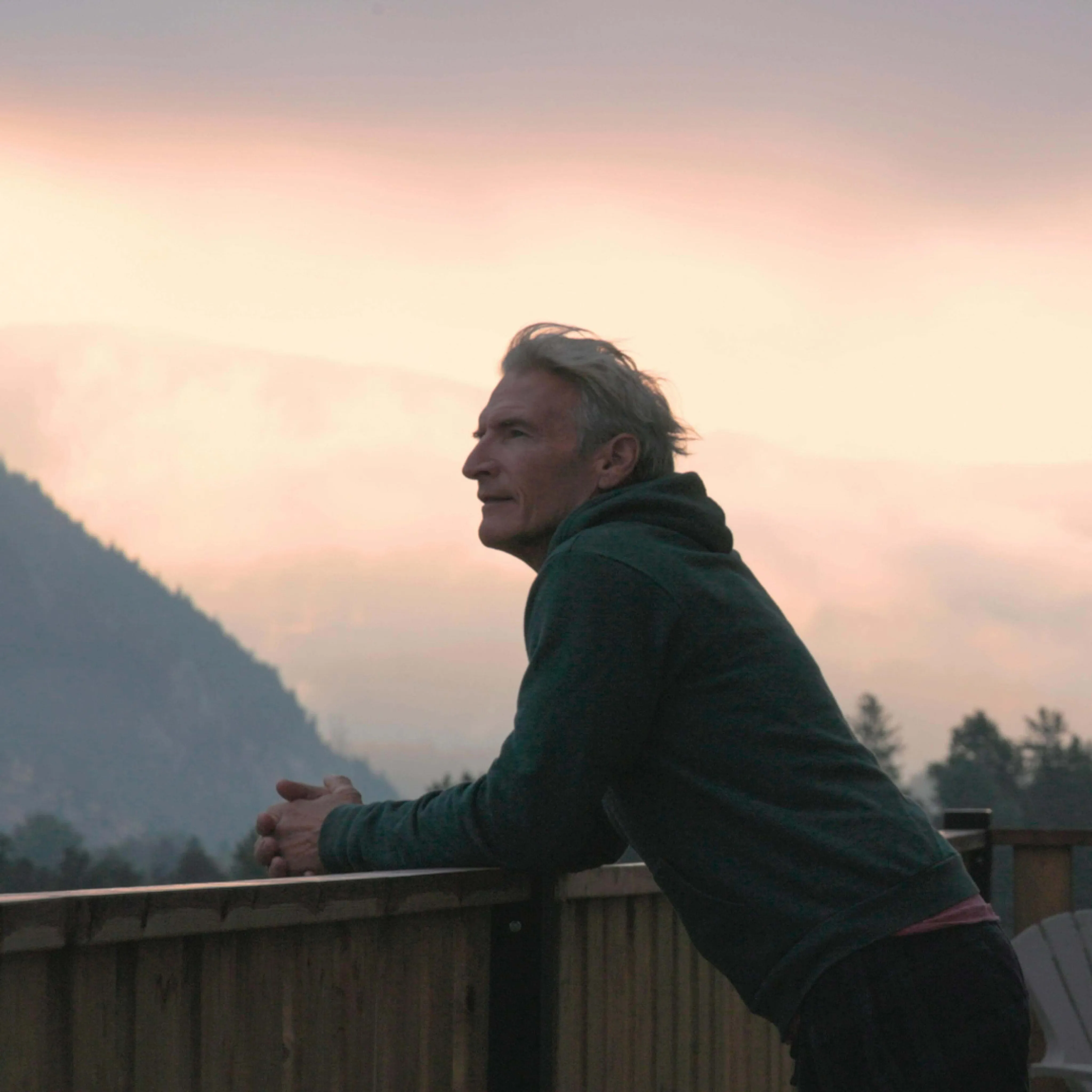 Older man on balcony watching sunset over mountains