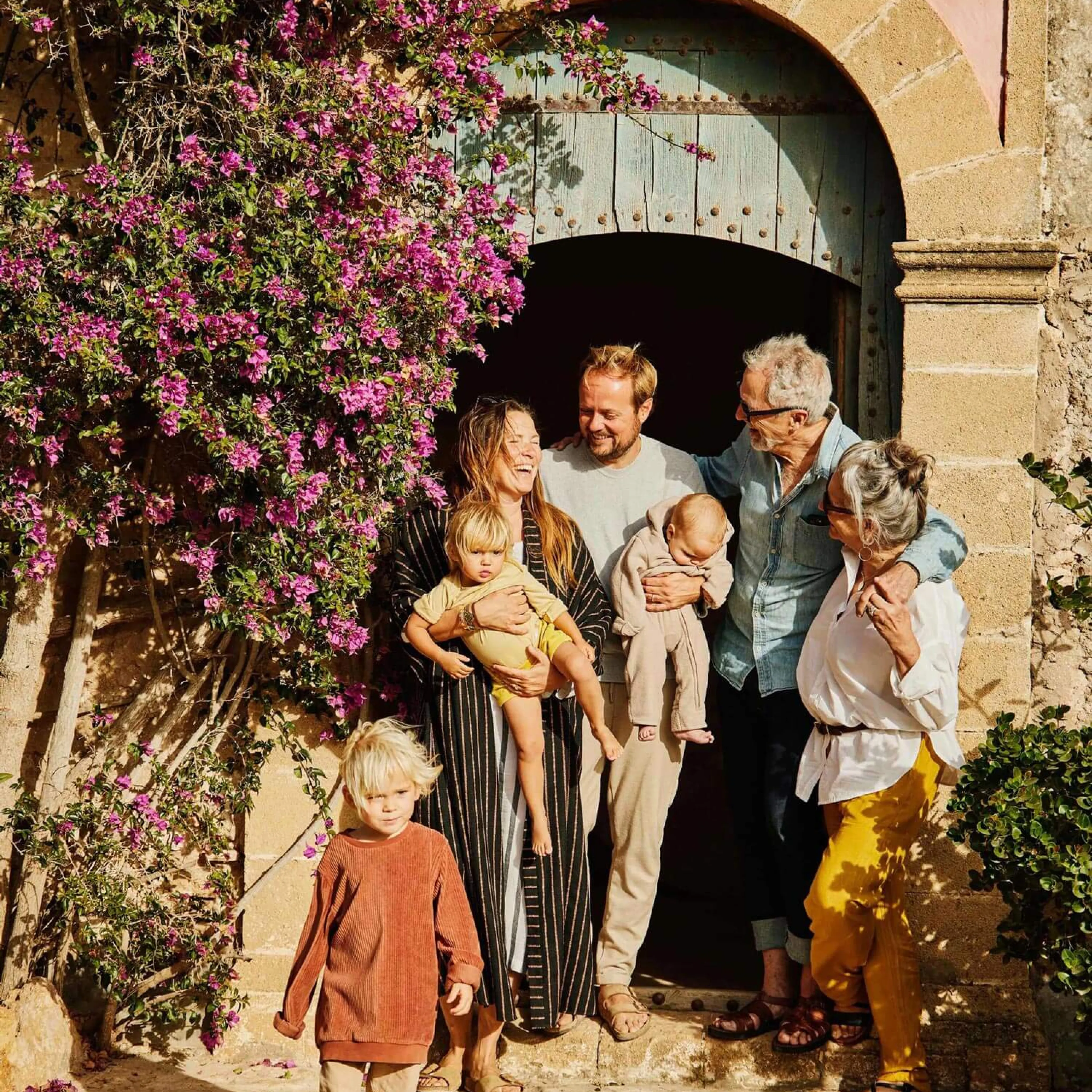 Family of seven laughing outside of a villa front door in the sunshine