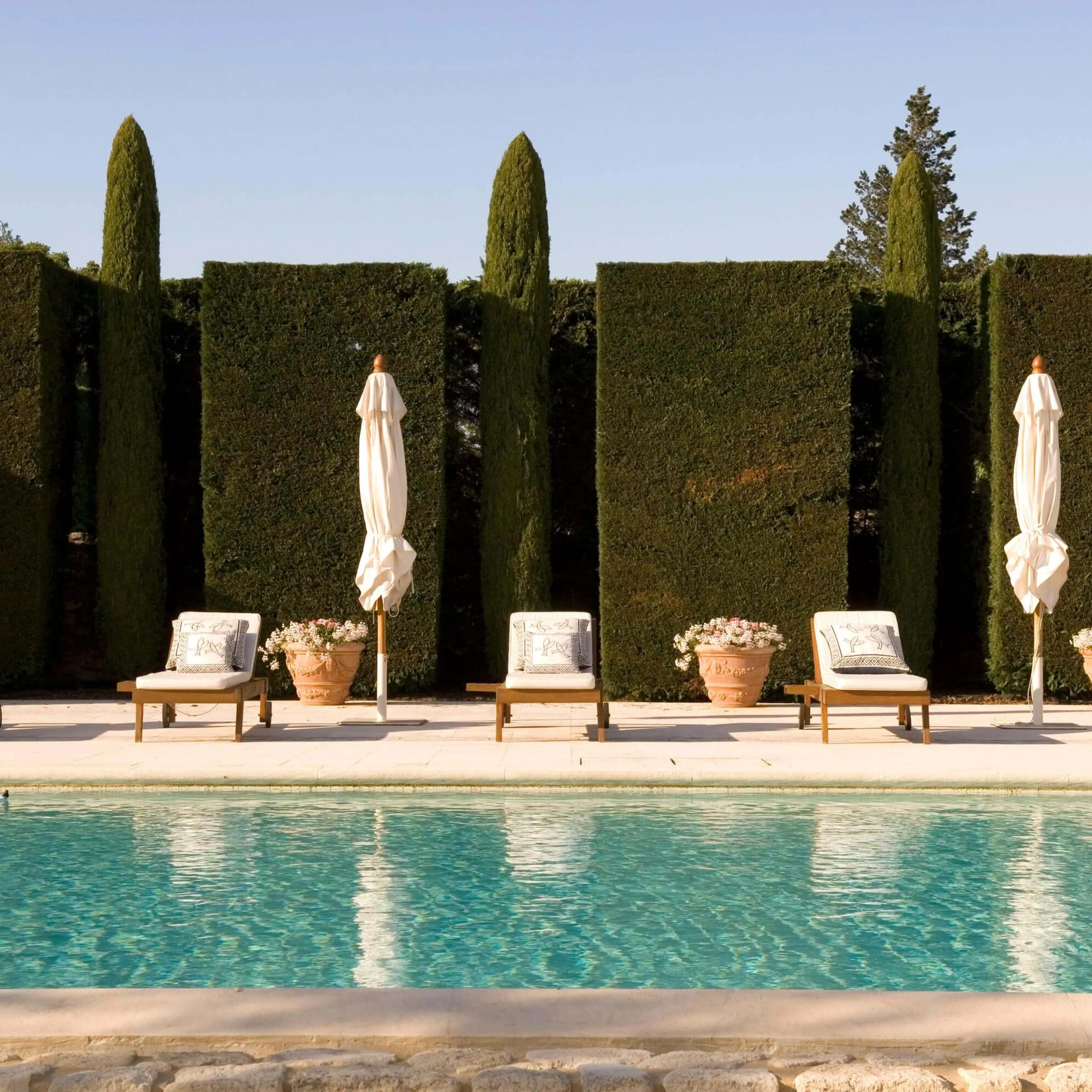 Five deck chairs and umbrellas lined up next to a pool