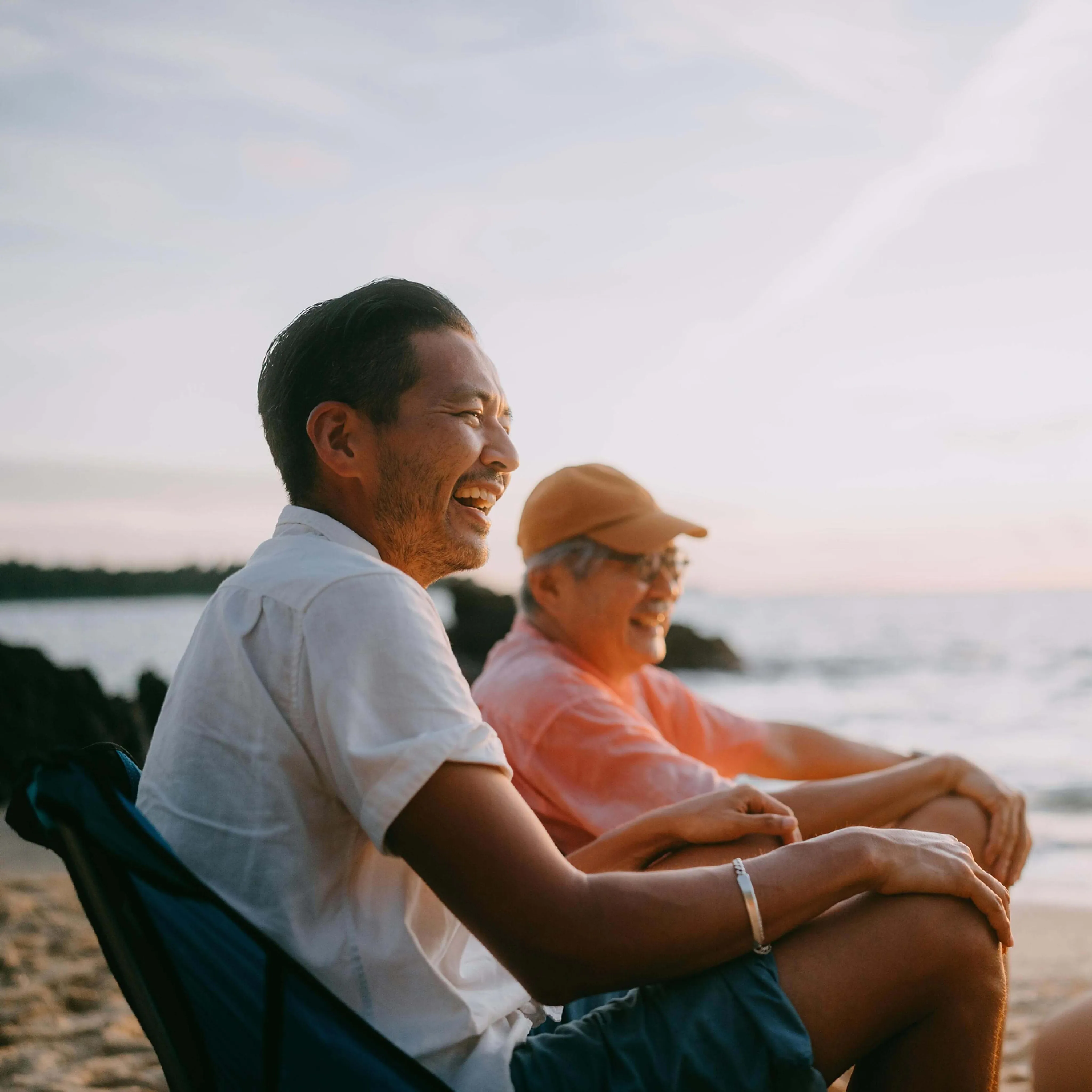 Father and son sitting on chairs and smiling at the beach in the afternoon sun