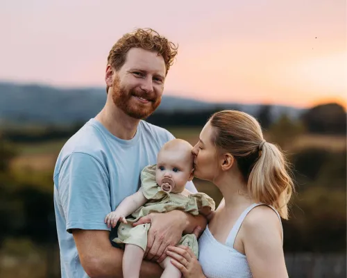 Young man and woman smiling and kissing new baby